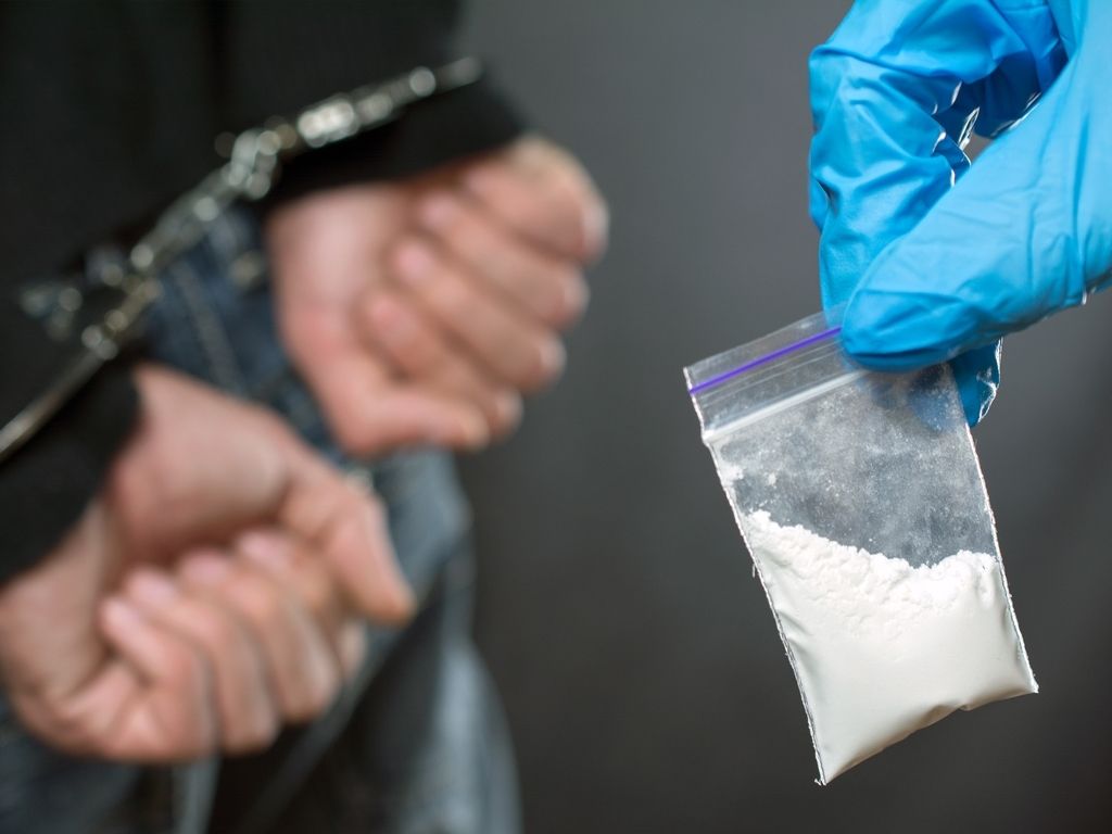 gloved hand holding cocaine in front of handcuffed person