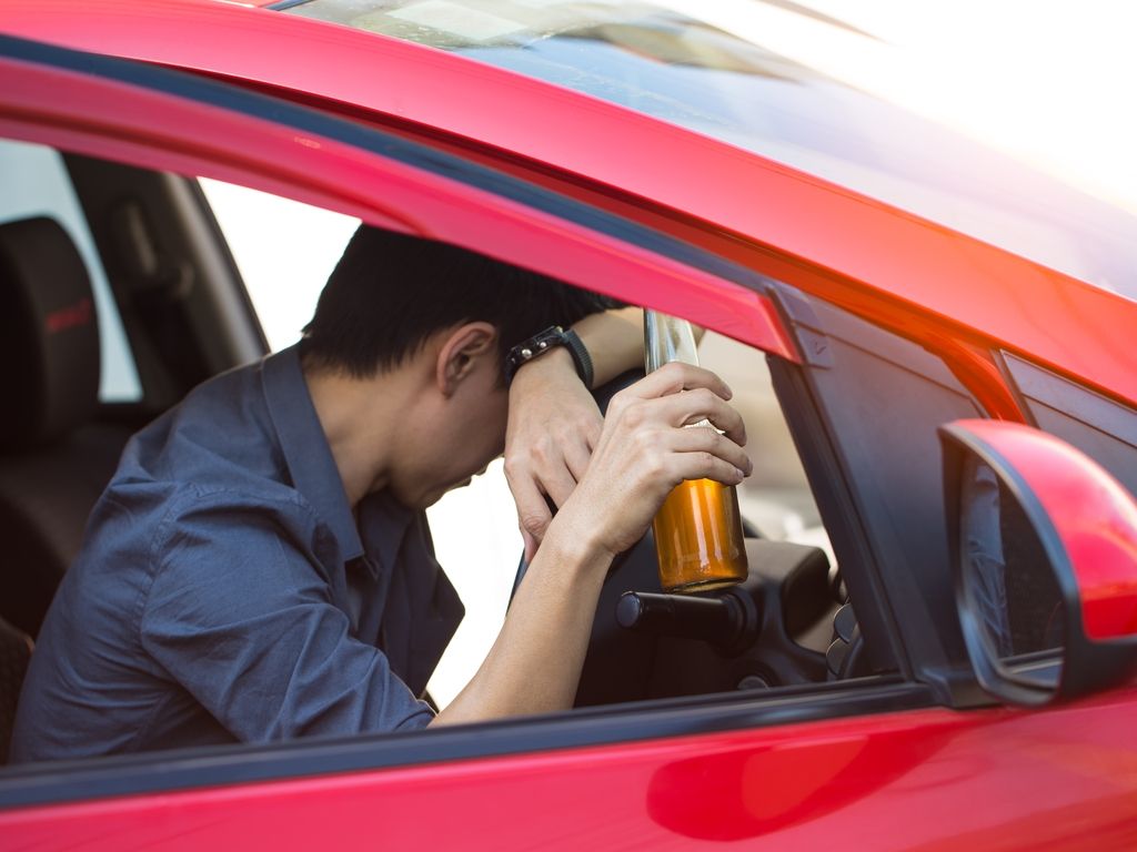 man leaning over steering wheel of a car with a beer in hand