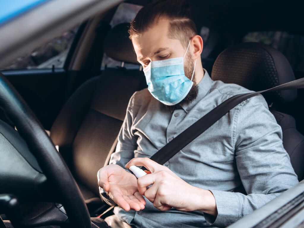 man using hand sanitizer in car while wearing a face mask